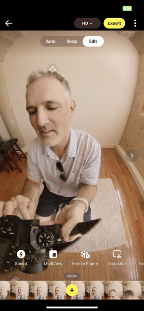 Selfie taken from above showing a man in a light blue shirt holding a camera, with wooden flooring and neutral walls visible.