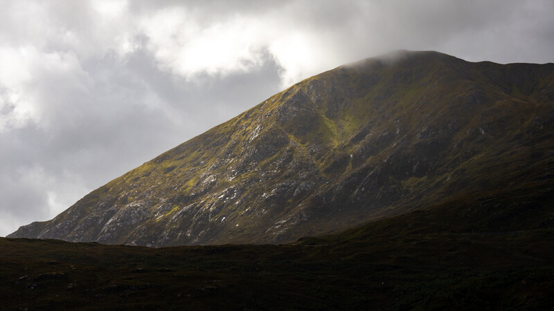Conical volcanic mountain with moss-covered slopes under overcast sky.