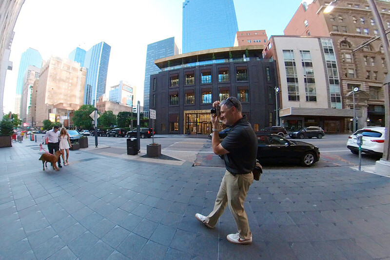 Urban street scene with pedestrian walking across paved plaza surrounded by tall buildings.