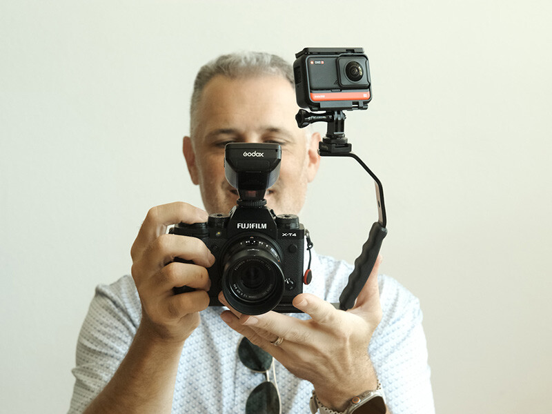 Photographer holding a Fujifilm camera with an action camera mounted on an articulating arm.
