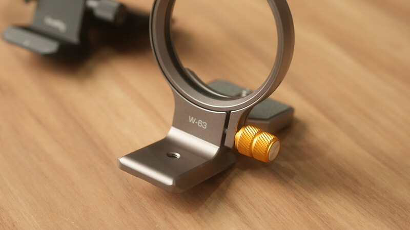 Camera lens mounting bracket with W-63 designation and gold adjustment knob on wooden surface