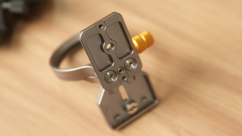 Close-up of a camera quick-release plate with brass connector and metal mounting bracket on wooden surface.