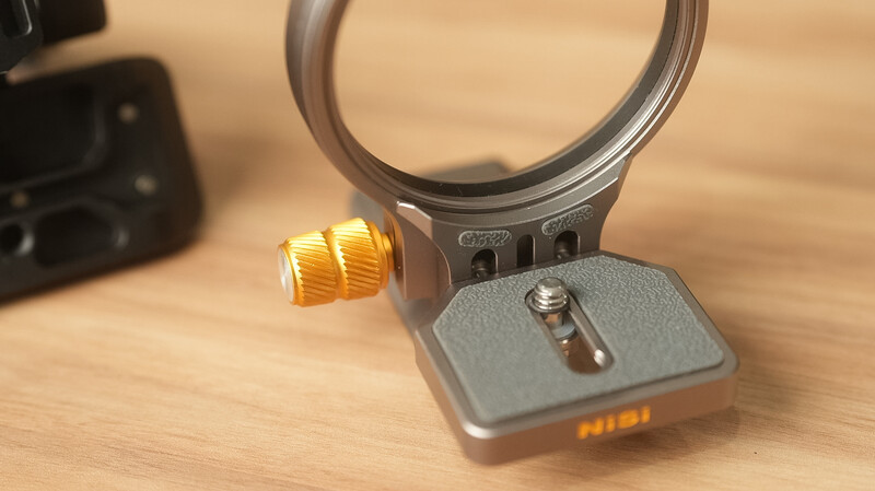 Camera quick-release plate with adjustable golden knob and mounting system on wooden surface.