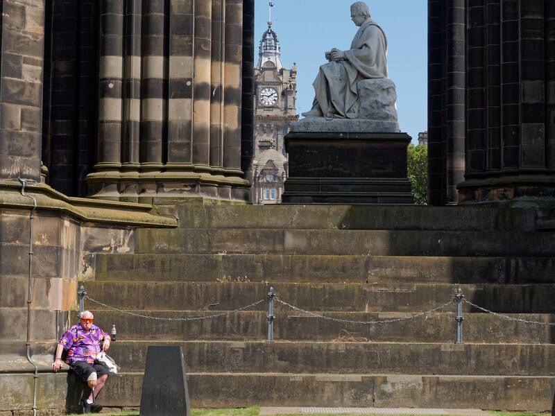 Person in purple jacket sitting on steps beneath classical stone architecture and statuary.