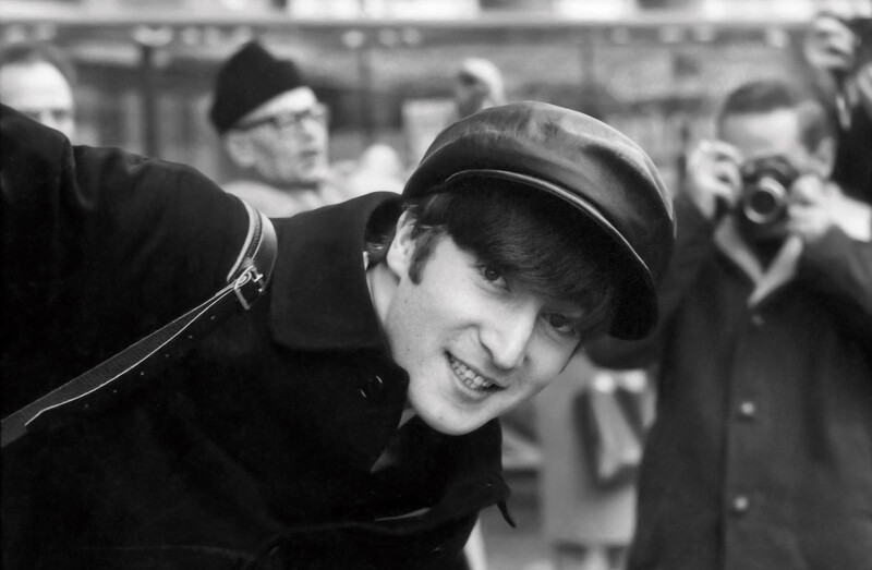 Portrait of John Lennon leaning in to the frame smiling at the camera