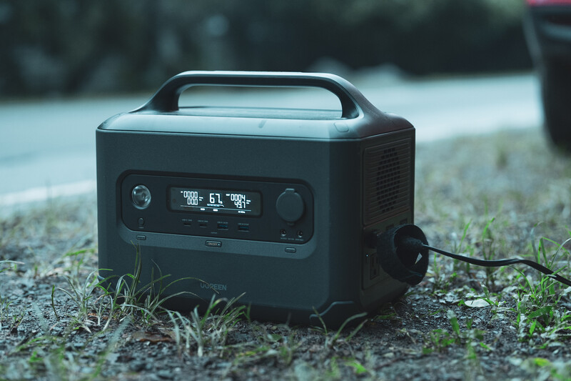 Portable power station with digital display sitting on pavement with grass and outdoor background.