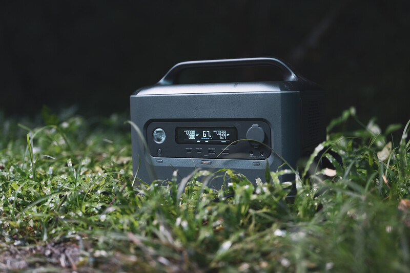 Portable Bluetooth speaker with digital display sitting in grass against dark background.