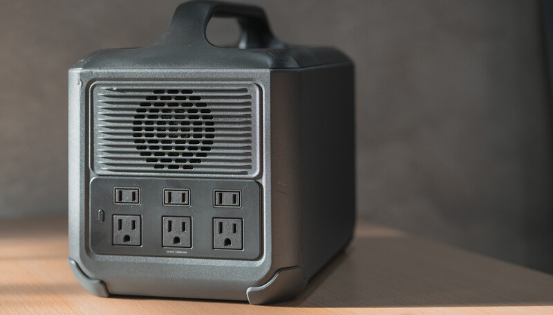 Compact portable power station with speaker grille and six electrical outlets arranged in two rows.
