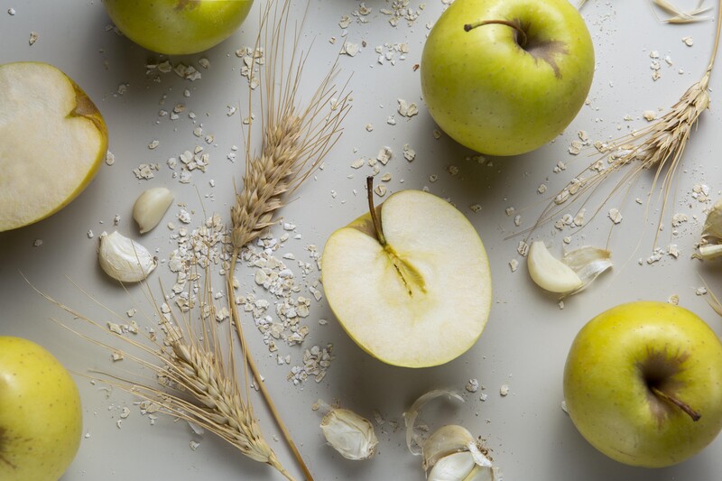 Green apples halved and whole arranged with wheat stalks and oats on neutral background.