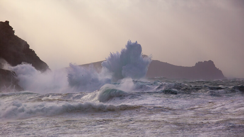 Dramatic coastal seascape with large waves crashing against rocky outcrops shrouded in mist.