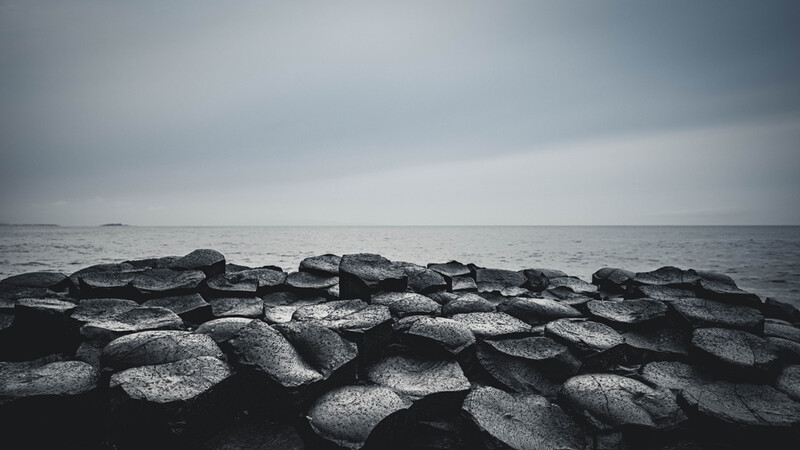 Rocky jetty extending into a gray, overcast seascape with calm waters.