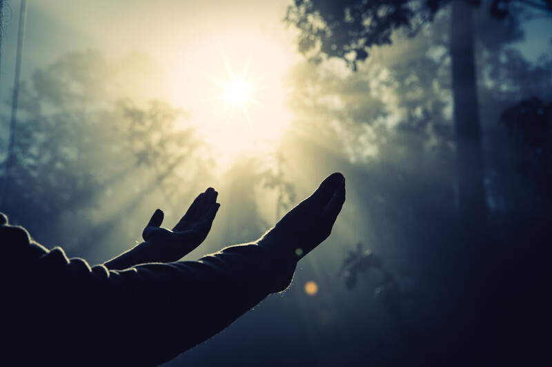 Silhouetted open hand against bright sun and sky with lens flare and dramatic clouds.