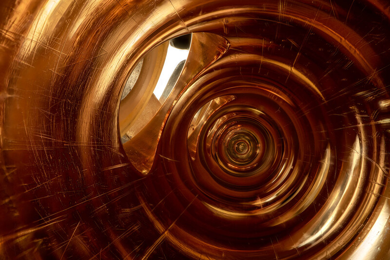 Concentric spiraling circles in warm bronze and gold tones converging toward a bright center point.