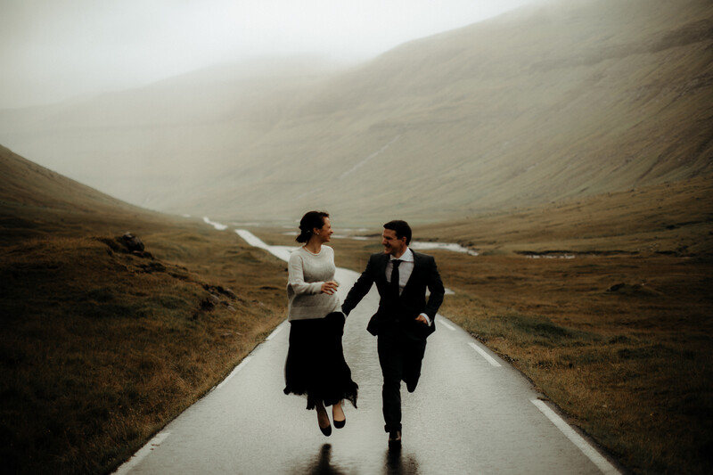 Couple running together down a wet road through a misty, barren mountainous landscape.