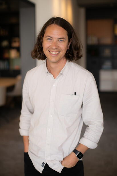 Person wearing white button-up shirt smiling at camera in indoor studio setting.