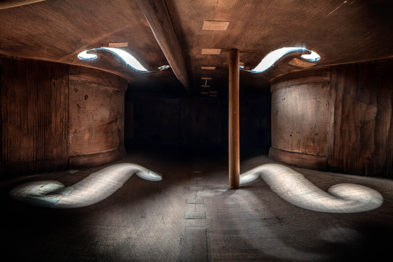 Symmetrical underground tunnel with mirrored curved white pipes and dramatic side lighting creating long shadows.