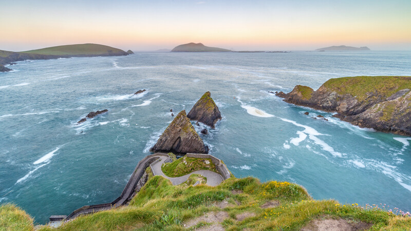 Coastal landscape with moss-covered sea stacks and distant islands at twilight.