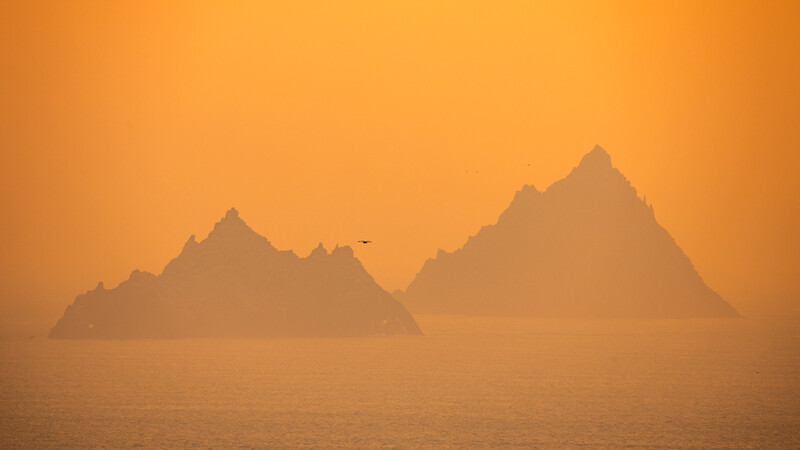 Two rocky islands silhouetted against a golden-orange sky, shrouded in atmospheric haze.