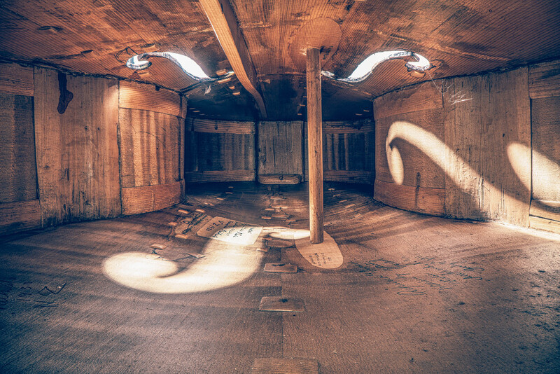 Abandoned industrial interior with natural light streaming through openings, casting geometric shadows across wooden floor.