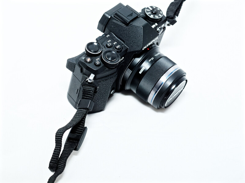 Black mirrorless camera with attached prime lens and camera strap on white background.