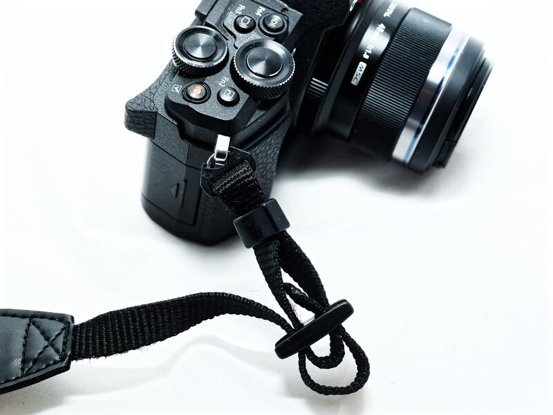 Mirrorless camera with attached lens and black camera strap on white background.