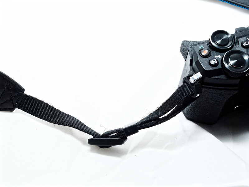 Black camera strap attached to a DSLR camera body with visible buttons and dials against white background.
