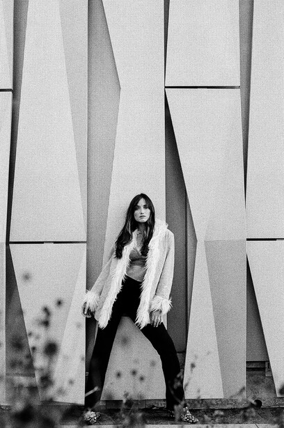 Woman in cardigan posing against geometric concrete wall panels in black and white.