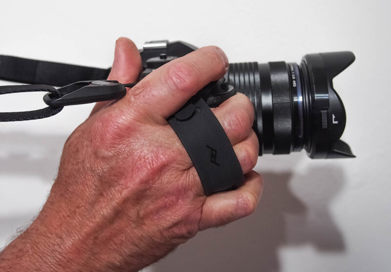 Hand holding a mirrorless camera with a black hand grip strap, demonstrating proper camera handling technique.