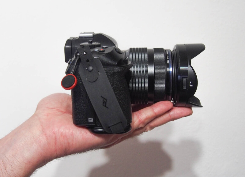 Compact mirrorless camera with attached lens held in an open palm against a neutral background.
