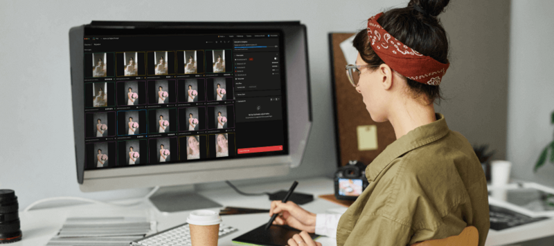 Photographer reviewing contact sheets on computer monitor while working at desk with tablet and stylus.