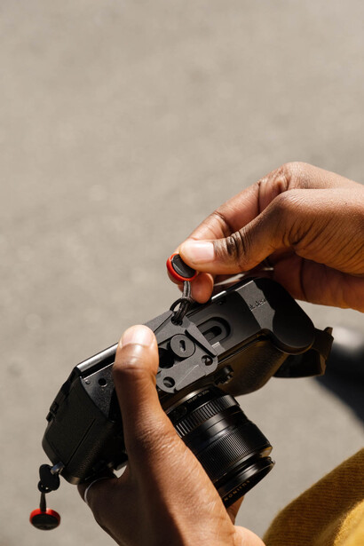 Photographer's hands holding a mirrorless camera with attached telephoto lens against neutral background.