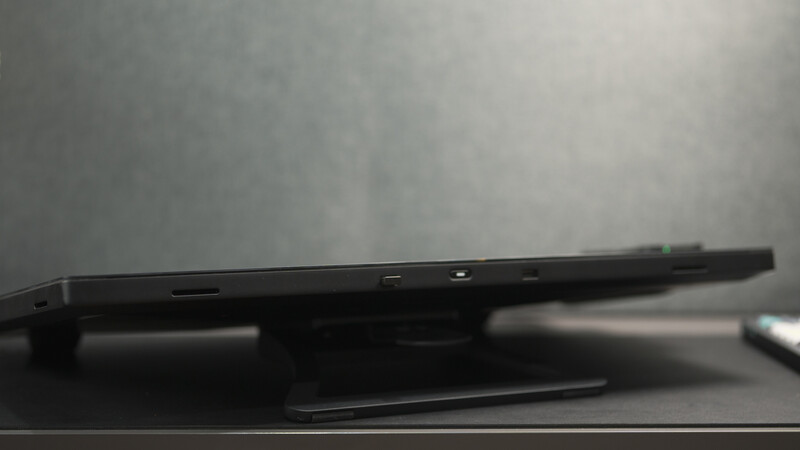 Black tablet device shown in profile against a blurred gray background.