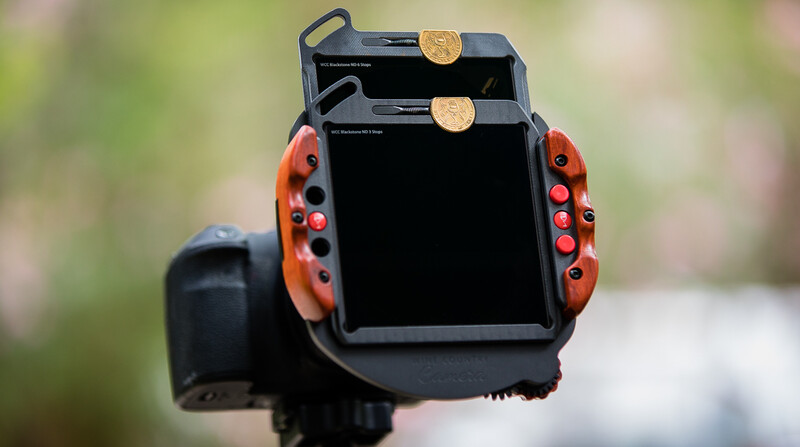 Thermal imaging camera with red grip handles and two pennies placed on top for scale reference.