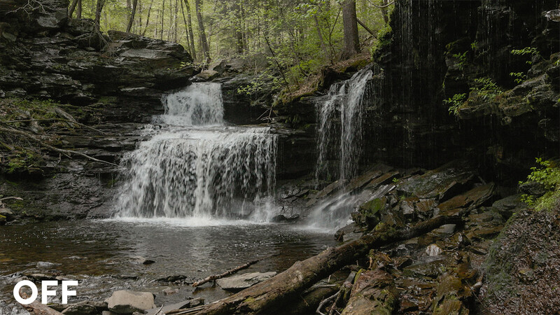 Multi-tiered waterfall cascading through moss-covered rocks in dense forest