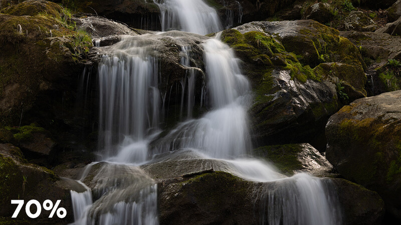 Cascading waterfall flowing over moss-covered rocks in a forest stream.