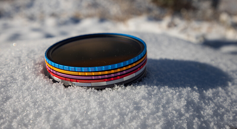 Colorful striped fabric bracelets stacked on snow with winter landscape in soft focus background.