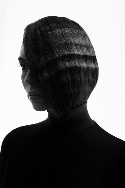 Profile view of a person with styled dark hair against a white background in high-contrast black and white lighting.