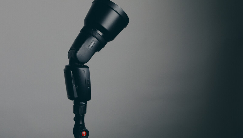 Professional camera flash mounted on articulating ball head against neutral gray background.
