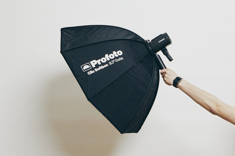 Hand holding a black Profoto octabox softbox against a neutral background.