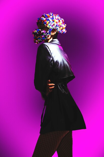 Silhouetted figure in black coat holding colorful bouquet against vibrant magenta background.