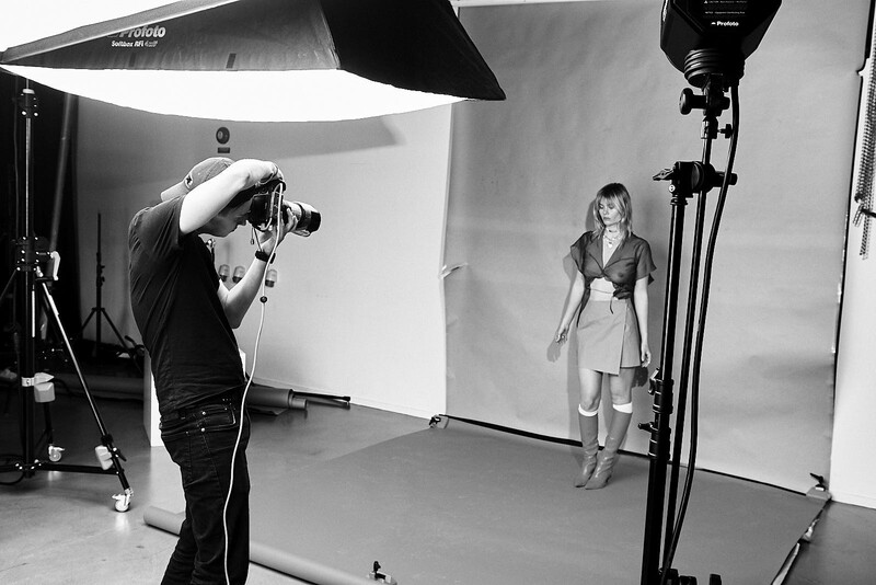 Photographer shooting a portrait of a woman in a professional studio with softbox lighting and white backdrop.