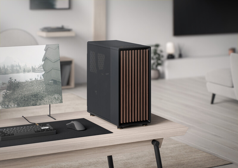 Black desktop computer tower with vertical slat design on wooden desk in bright studio workspace.