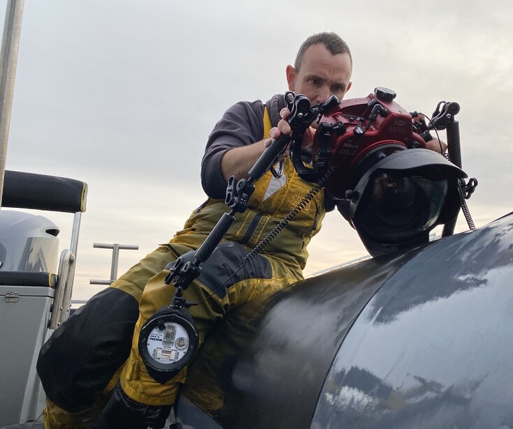 Photographer in yellow jacket operating camera mounted on motorcycle engine.