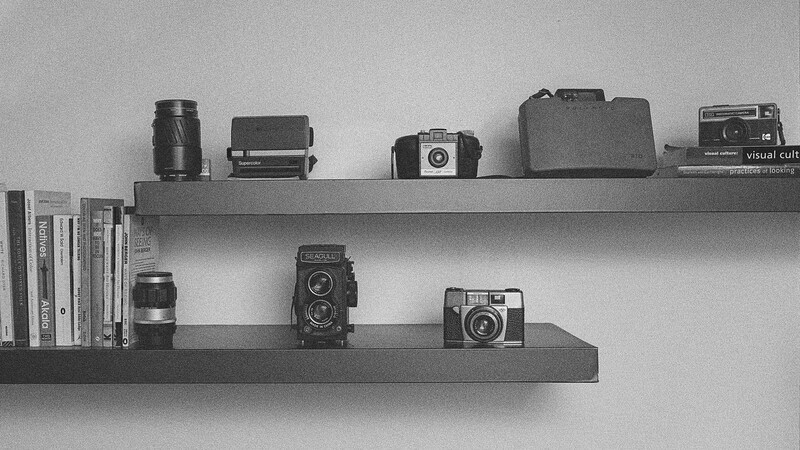 Two floating shelves displaying vintage cameras, lenses, and photography books in black and white.