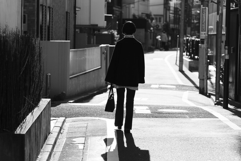 Man in dark suit walking away down a sunlit urban alley, shot from behind in black and white.
