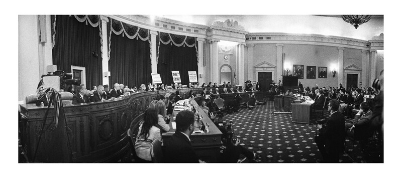 Black and white photograph of a formal legislative or governmental assembly hall with rows of seated attendees and elevated speaker's platform.