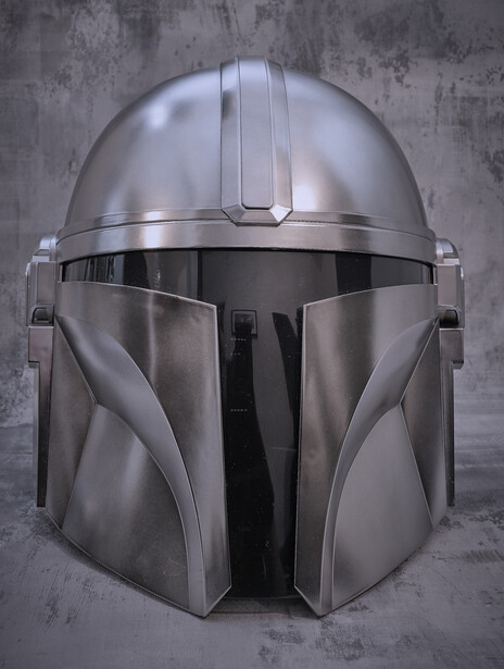 Metallic helmet with angular design and front-facing visor against textured gray background.