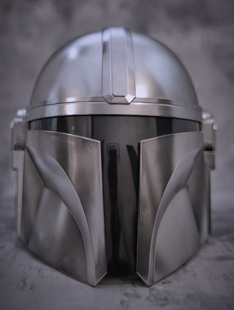 Polished metallic helmet with angular design and vertical center ridge, photographed against neutral gray background.
