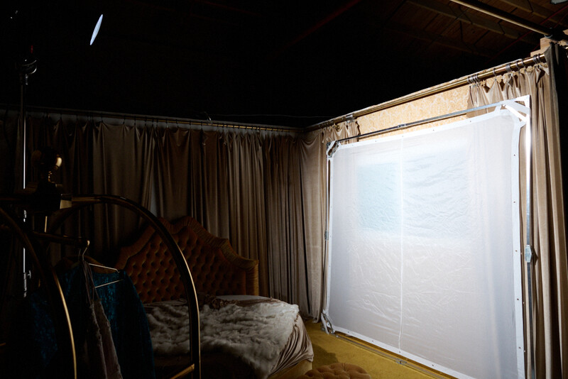 Studio setup with large softbox key light illuminating a bed with patterned bedding against dark backdrop.