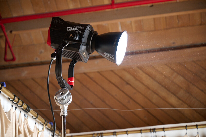 Professional film light mounted on a C-stand with reflector attachment in a gymnasium.